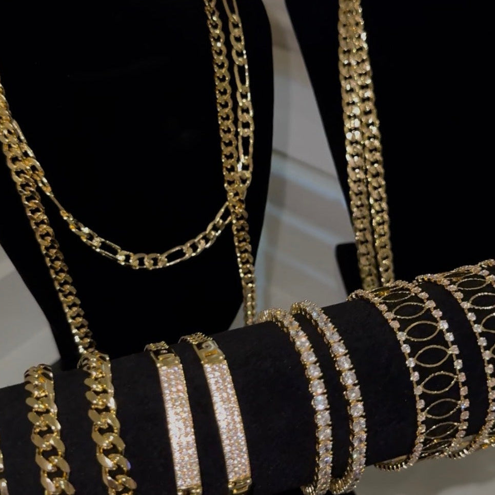 Gold-toned chain necklaces and matching bracelets displayed on black velvet jewelry busts, with some pieces set in clear stones, photographed indoors.